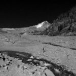 Hiker crosses a wide gully with braided streams on the south side of Mount Hood. Mount hood, a pyramid standing above the hiker.